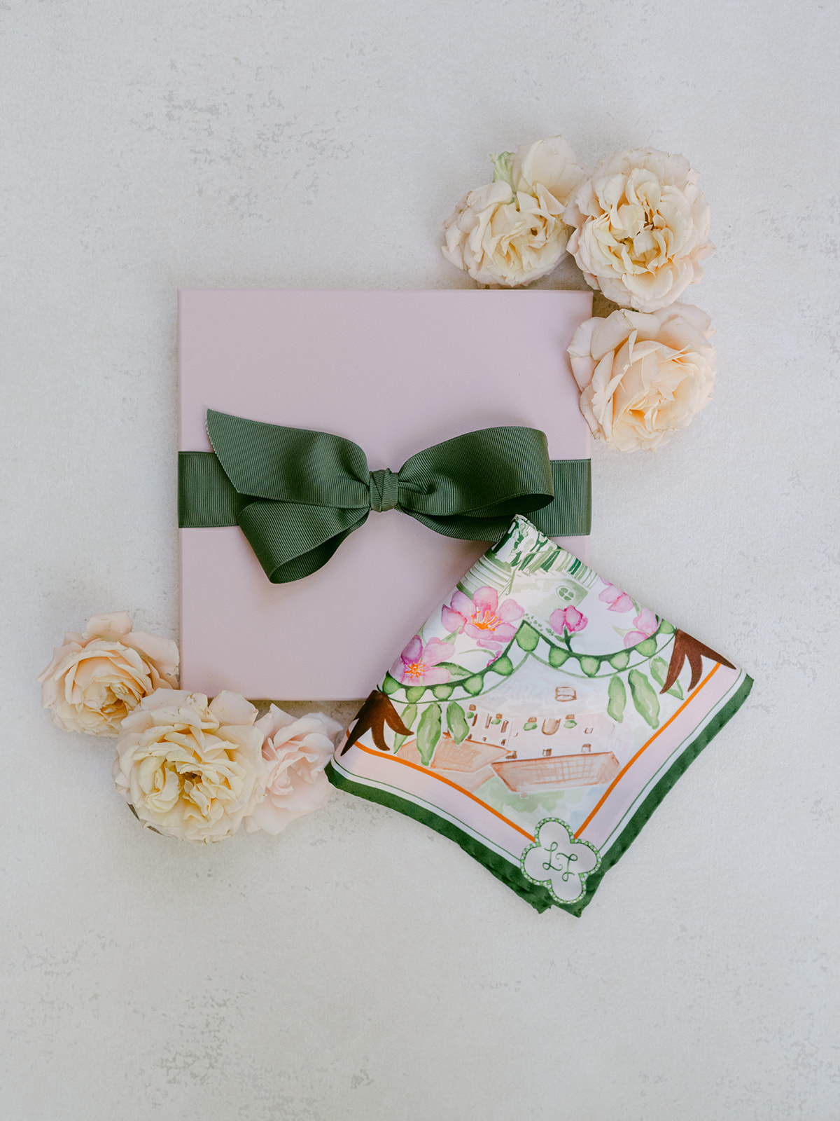 A custom silk pocket square wedding favor beside its pale pink gift box, the couple's monogram printed in the corner