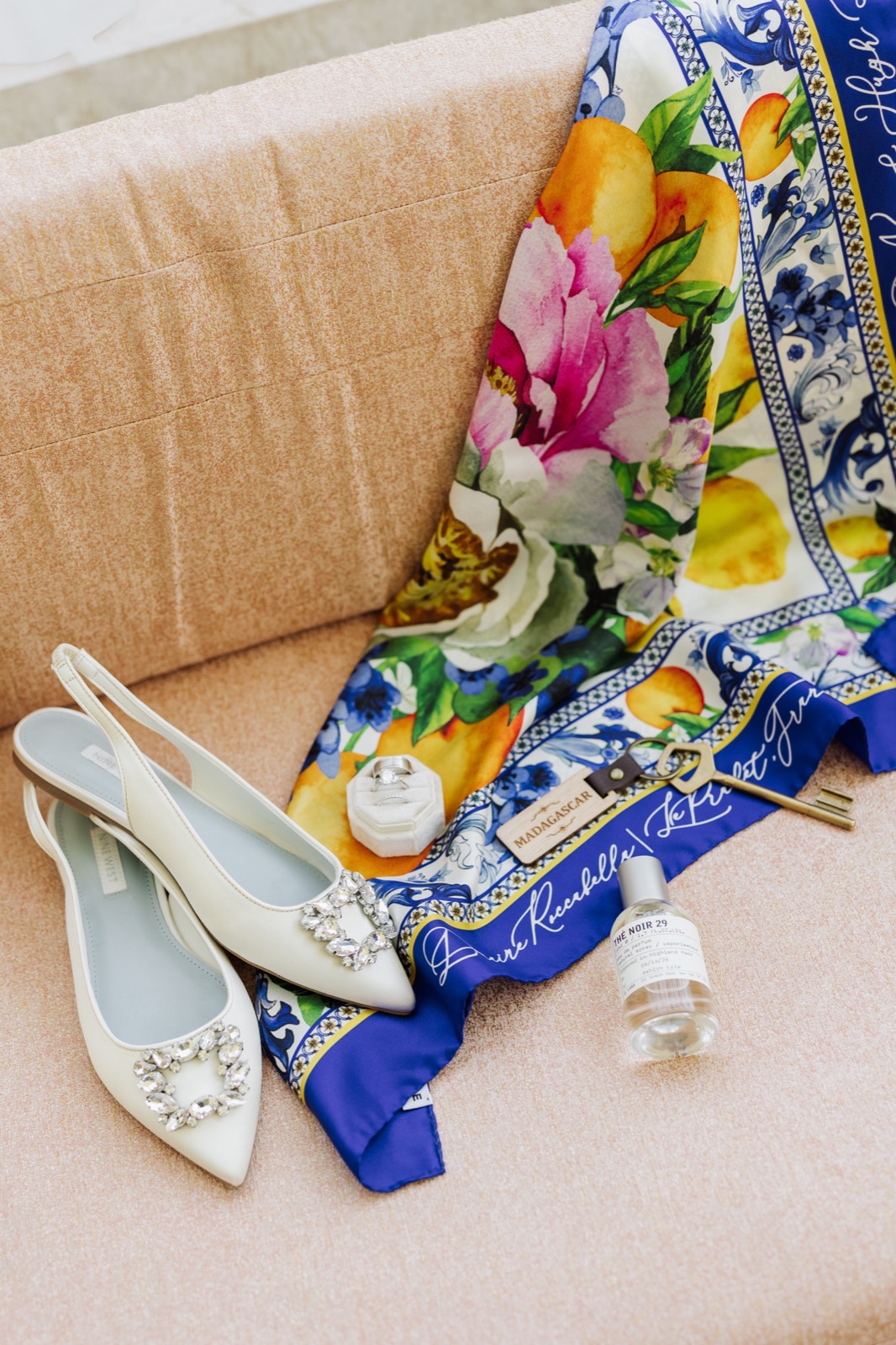 A personalized silk wedding invitation scarf draped over a chair with the bride's shoes, rings and perfume