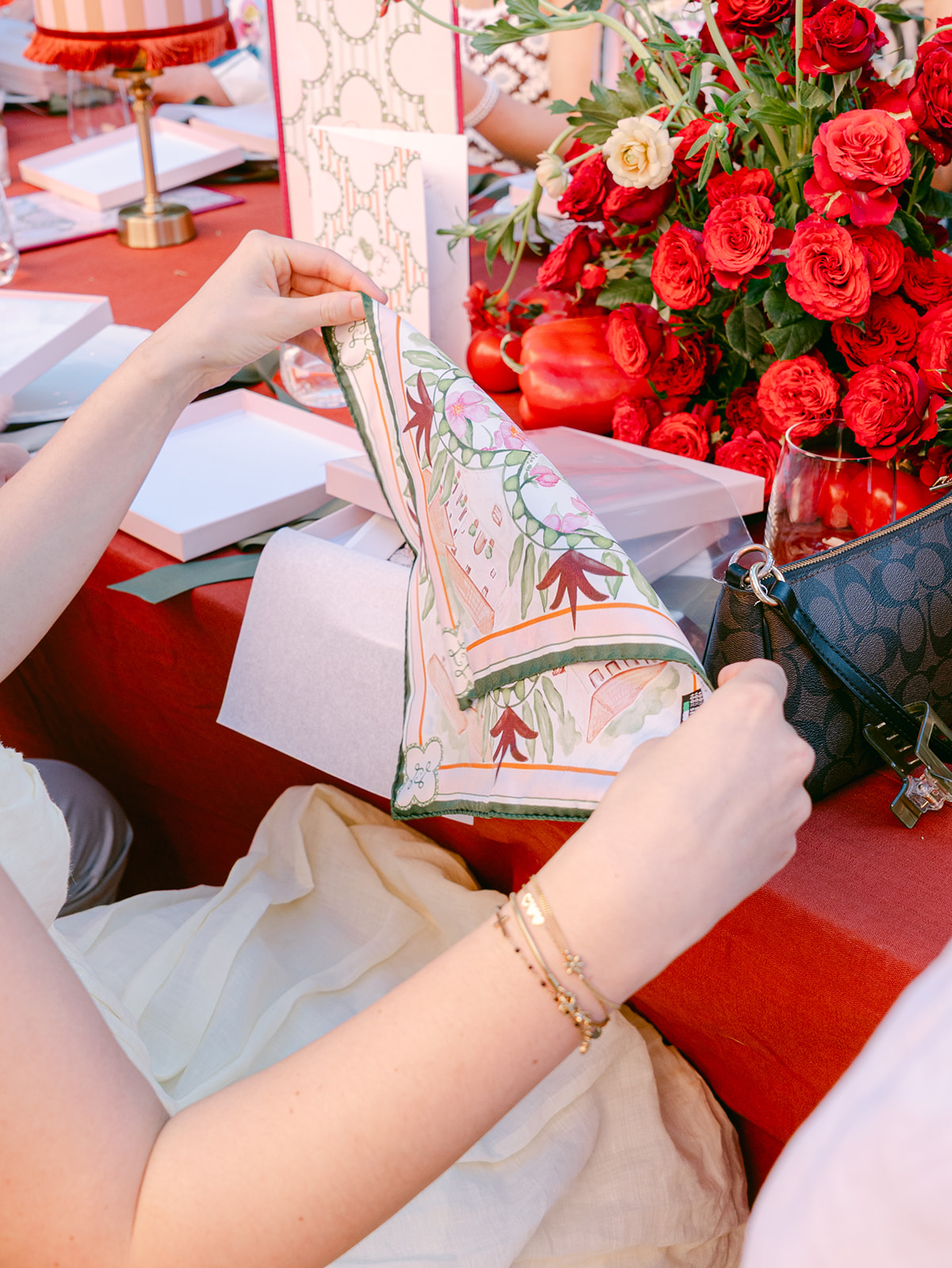 A wedding guest lifts a custom silk pocket square out of its box at the dinner table